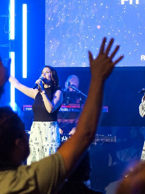 People with their hands up in praise and a woman singing on stage